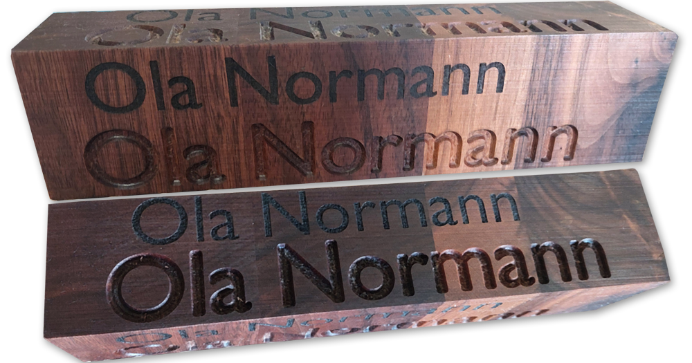 Eksempel på forskellen mellom lasergravert og CNC-gravert tekst i valnøtt. Laser på øverste linje og CNC under.